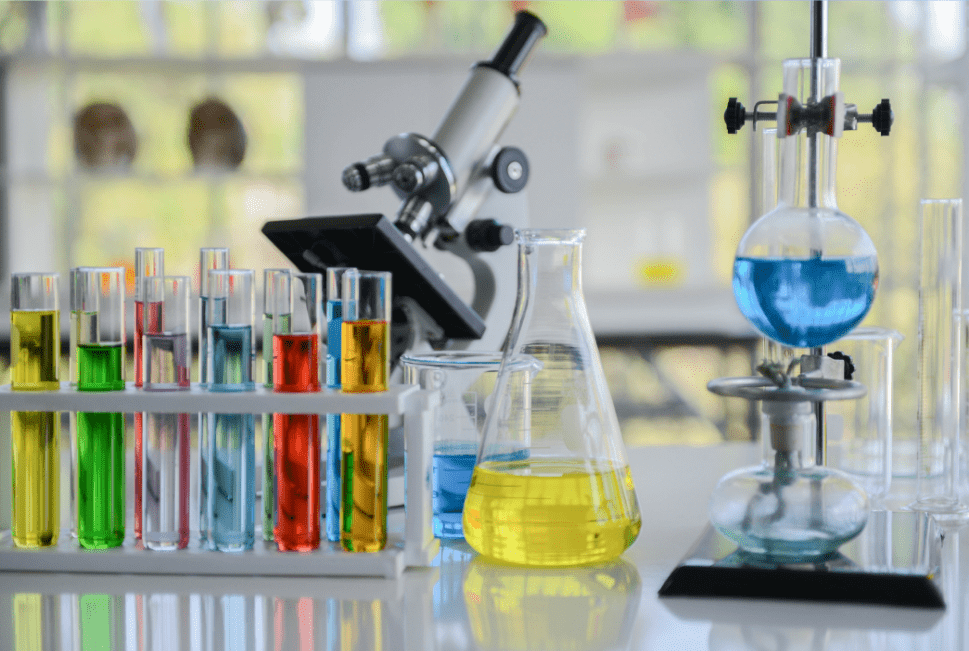 Chemistry lab setup with test tubes containing colorful liquids, a microscope, conical flask with yellow solution, and round-bottom flask heated over a burner
